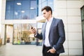 Happy smiling businessman wearing suit and using modern smartphone near skyscraper office Royalty Free Stock Photo