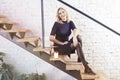 Happy smiling businesswoman sitting on stairs in modern office, working at laptop and having coffee, sunshine daylight. Royalty Free Stock Photo