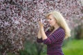 Happy smiling Caucasian blond woman with long hair smiles and happy near blossoming plum cherry tree, enjoys the blossom Royalty Free Stock Photo