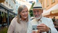 Happy smiling Caucasian senior elderly couple walking taking selfie laughing talking gadget mobile phone together city Royalty Free Stock Photo
