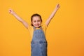 Happy smiling cheerful preschool girl, clenching fists and raising arms, expressing positive emotions isolated on orange
