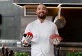 Happy smiling chef prepares meat dish with various vegetables in the kitchen. In one hand the man holds vegetables, in the other a Royalty Free Stock Photo