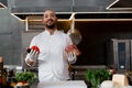 Happy smiling chef prepares meat dish with various vegetables in the kitchen. In one hand the man holds vegetables, in the other a Royalty Free Stock Photo