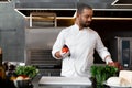 Happy smiling chef prepares meat dish with various vegetables in the kitchen. In one hand the man holds vegetables, in the other a Royalty Free Stock Photo