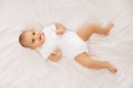 Happy, smiling child, baby, adorable girl in white onesie lying on bed and lookin upwards against white background Royalty Free Stock Photo