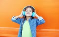 Happy smiling child enjoys listens to music in headphones over colorful orange