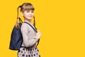Happy smiling child girl is going to school for the first time. Child with school bag and with funny pigtails isolated on yellow