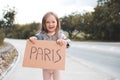 Happy smiling child girl 3-4 year old hold paper craft Paris handwritten sign hitch hiking on road outdoors. Happiness. Royalty Free Stock Photo