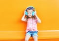 Happy smiling child listens to music in headphones over colorful orange