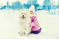 Happy smiling child with white Samoyed dog playing on snow in winter Royalty Free Stock Photo