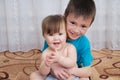 Happy smiling children portrait. Siblings - boy holding little baby girl, together sitting home