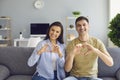 Happy smiling couple holds hands in the shape of a heart welcomes sitting in the house