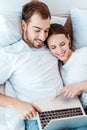 Smiling couple lying on bed and using laptop Royalty Free Stock Photo