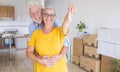 Happy smiling couple of senior people white hair hugging  holding the keys of the new empty apartment with moving boxes on the Royalty Free Stock Photo