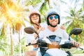 Happy smiling couple travelers riding motorbike scooter in safety helmets during tropical vacation under palm trees Royalty Free Stock Photo