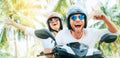 Happy smiling couple travelers riding motorbike scooter in safety helmets during tropical vacation under palm trees on Ko Samui Royalty Free Stock Photo