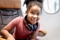 Happy smiling curly hair African girl child passenger with headphones sitting in seat next to window inside airplane, cheerful kid Royalty Free Stock Photo