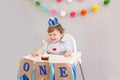 Happy smiling cute Caucasian baby boy in blue crown celebrating first birthday at home. Child kid toddler sitting in high chair Royalty Free Stock Photo