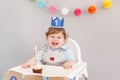 Happy smiling cute Caucasian baby boy in blue crown celebrating his first birthday at home. Child kid toddler sitting in high Royalty Free Stock Photo