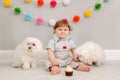 Happy smiling cute Caucasian baby boy celebrating first birthday at home. Child kid toddler sitting on floor with two white pet Royalty Free Stock Photo