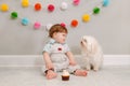 Happy smiling cute Caucasian baby boy celebrating first birthday at home. Child kid toddler sitting on floor with white pet dog. Royalty Free Stock Photo
