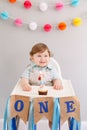 Happy smiling cute Caucasian baby boy celebrating first birthday at home. Child kid toddler sitting in high chair eating tasty Royalty Free Stock Photo