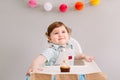 Happy smiling cute Caucasian baby boy celebrating his first birthday at home. Child kid toddler sitting in high chair eating tasty Royalty Free Stock Photo