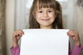 Happy smiling cute child girl holding white copy space sheet of drawing paper. Art education, creativity, advertisement concept Royalty Free Stock Photo