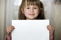 Happy smiling cute child girl holding white copy space sheet of drawing paper. Art education, creativity, advertisement concept Royalty Free Stock Photo