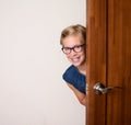 Happy smiling cute girl in eyeglasses behind door at home.