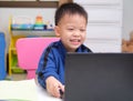Happy smiling cute little Asian kid with notebook laptop computer making video call at home, Kindergarten boy studying online, Royalty Free Stock Photo