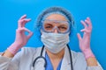 Happy smiling doctor in protective mask and glasses. The nurse laughs with her hands up, a portrait on a blue background Royalty Free Stock Photo