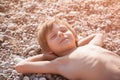 Happy smiling dreaming little kid with brown skin lying on pebble beach during leisure sunbathe tan