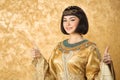 Happy smiling Egyptian woman like Cleopatra with thumbs up gesture, on golden background Royalty Free Stock Photo