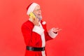 Happy smiling elderly man with gray beard wearing santa claus costume talking phone, speaking with Royalty Free Stock Photo