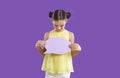 Happy smiling elementary school girl with text bubble standing on purple studio background. Royalty Free Stock Photo