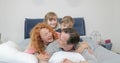 Happy smiling family in bedroom children and parents communication lying together on father on bed in morning