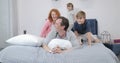 Happy smiling family having fun in bedroom lying together on father on bed in morning