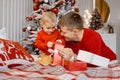 Happy smiling father and his impatient little son unwrapping a present sitting on the bed near Christmas tree Royalty Free Stock Photo