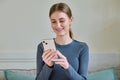 Happy female teenager using smartphone, sitting on couch at home Royalty Free Stock Photo