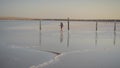 Slim girl enjoying sunset, walks between wooden salt pillars of a salt lake