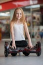 Happy and smiling girl with mini segway at trading mall. Teenager riding on hover board or gyroscooter.