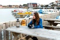 Happy smiling girl traveler drinks warm tea at the rustic wooden table outdoor near the traditional fishing houses Rorbu and Royalty Free Stock Photo