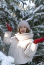 Happy smiling girl in a warm hat stands among the pine trees. Sunny winter day Royalty Free Stock Photo