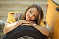 Happy smiling girl is wearing yellow sweater is posing with auto wheel near old retro bus, autumn concept Royalty Free Stock Photo