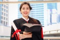 Happy smiling graduated student, young beautiful Asian woman holding square academic hat cap and certificate, standing with arms Royalty Free Stock Photo