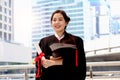 Happy smiling graduated student, young beautiful Asian woman holding square academic hat cap and certificate, standing with arms Royalty Free Stock Photo