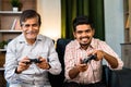 Happy smiling grandfather and grandson playing video game using game pad by looking camera at home - concept of Royalty Free Stock Photo