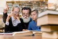 Happy smiling grandfather reading book with grandson and granddaughter, sitting at the table in old vintage library