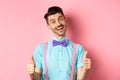 Happy smiling guy in bow-tie and suspenders showing thumbs up, praising good job, approve nice work, standing over pink Royalty Free Stock Photo